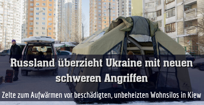 Zelte zum Aufwärmen vor beschädigten, unbeheizten Wohnsilos in Kiew