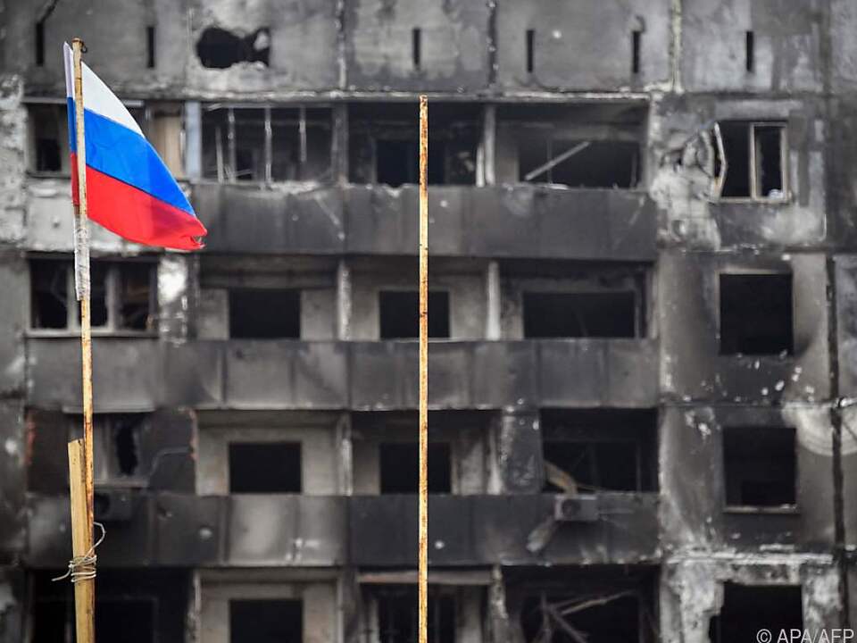 Russische Flagge vor zerstörtem Gebäude in Mariupol